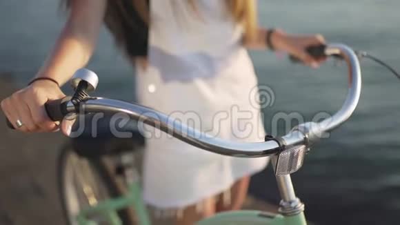 在自行车车把上的女性手特写镜头日落或日出时海上迷人的年轻女子视频的预览图