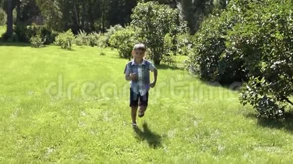 一个有魅力的男孩在阳光明媚的天气里沿着公园的草地跑步心情很好慢动作高清高清视频的预览图