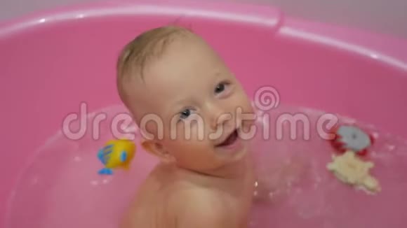 可爱的婴儿在浴室游泳可爱的小婴儿沐浴在粉红色的浴缸里视频的预览图
