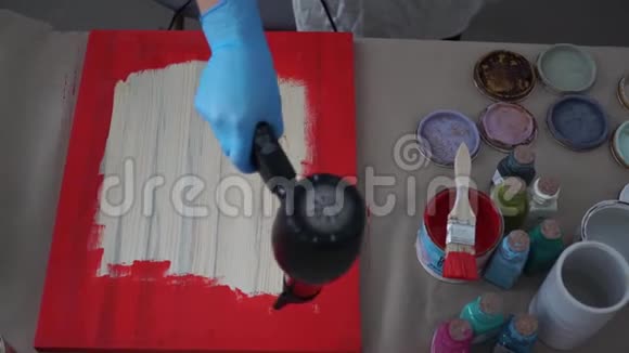 女孩用吹风机在围裙和手套上擦干一张照片油漆罐视频的预览图