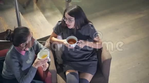 两个浅黑肤色的年轻女孩坐在椅子上一边聊天一边喝茶视频的预览图