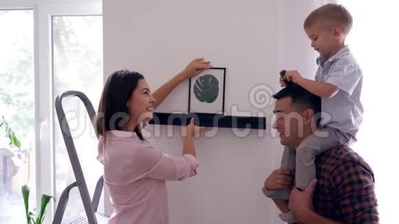 在公寓装修期间一对年轻夫妇带着小男孩在墙上挂画视频的预览图