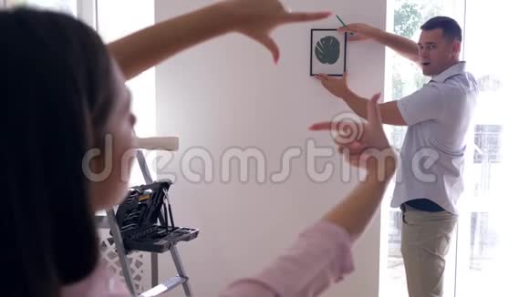 重新装饰美丽的男人挂在墙上而女性用手指做框架决定在墙上装饰视频的预览图