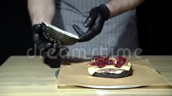 厨师的双手烹饪一个美味的黑汉堡与烟熏培根和樱桃酱视频的预览图