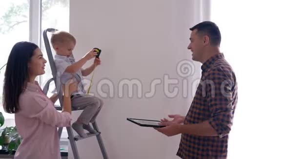 年轻的家庭在新公寓的室内装修中很开心开朗的父亲和儿子妻子亲吻丈夫视频的预览图