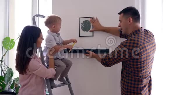 带卷尺的漂亮孩子在修理后帮爸爸妈妈把架子挂在墙上视频的预览图