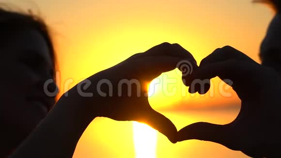 幸福的年轻夫妇在日落时用手在海洋上做心形日落海上的男人和女人剪影视频的预览图