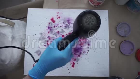 女孩用吹风机在围裙和手套上擦干一张照片油漆罐视频的预览图