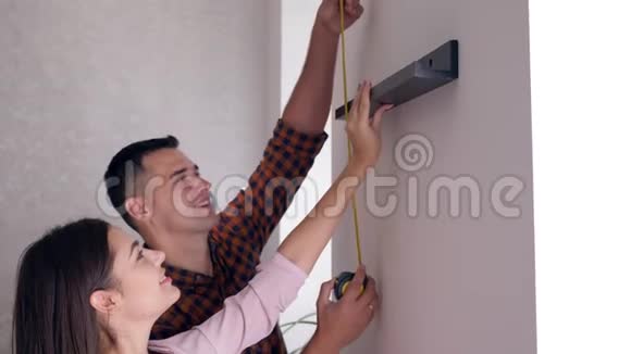 正婚夫妇手拿卷尺公寓维修后挂在墙上视频的预览图