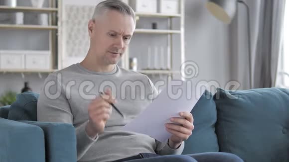 白发人坐沙发纸工时阅读文件视频的预览图