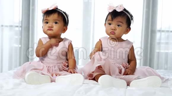 两个穿着粉红色裙子的双胞胎宝宝躺在床上一个在看一个在哭视频的预览图
