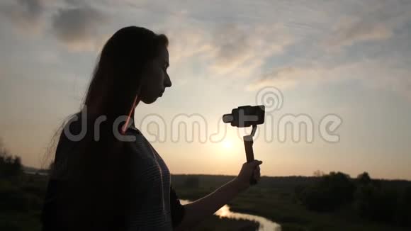 漂亮女孩在日落时分用稳定器在手机上拍摄视频慢动作视频的预览图