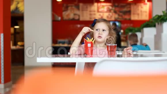 小女孩在咖啡馆里吃快餐炸薯条和喝果汁视频的预览图