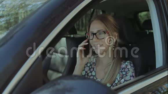 积极的女人在车里用智能手机说话视频的预览图