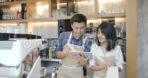 两位年轻的亚洲咖啡师男女在咖啡店休息时使用平板电脑视频的预览图