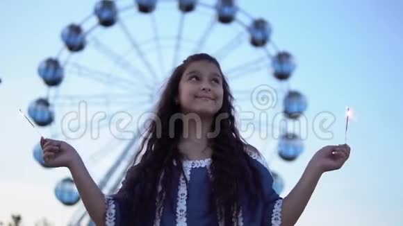 女孩手里拿着烟花站在摩天轮的背景上高兴慢动作视频的预览图