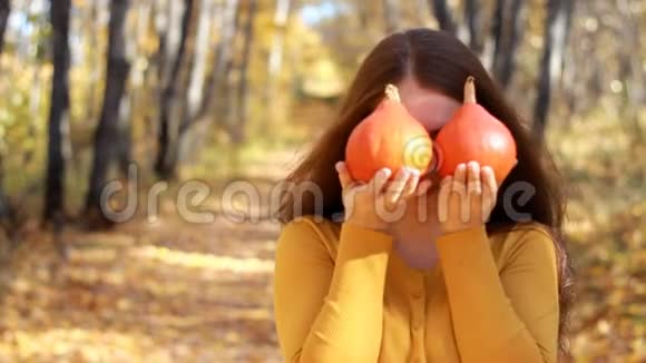 女人手里拿着小南瓜在一个秋天阳光明媚的日子里森林里有黄色和金色的叶子视频的预览图