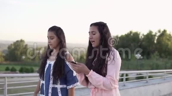 两个女朋友沿着街走用智能手机聊天慢动作视频的预览图