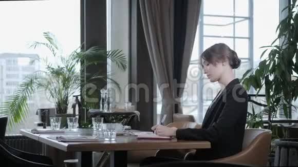 女人在笔记本上做笔记的特写年轻的女商人坐在木桌旁的咖啡店里视频的预览图