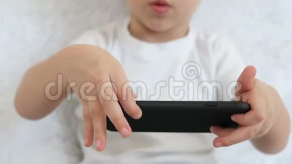 一个孩子拿着一部智能手机在他面前在白色背景下缓慢地玩游戏一幅肖像画视频的预览图