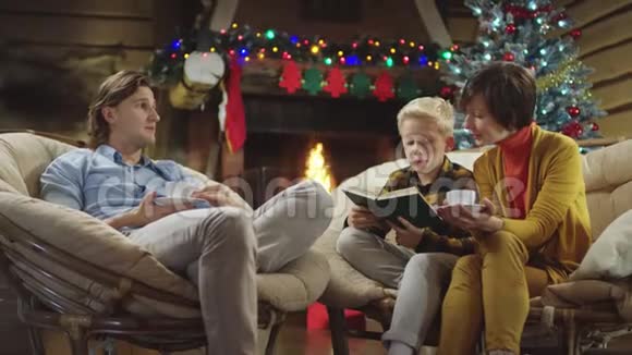 年轻人和他的母亲一边喝咖啡一边说话小男孩一边读一本关于圣诞节的书视频的预览图