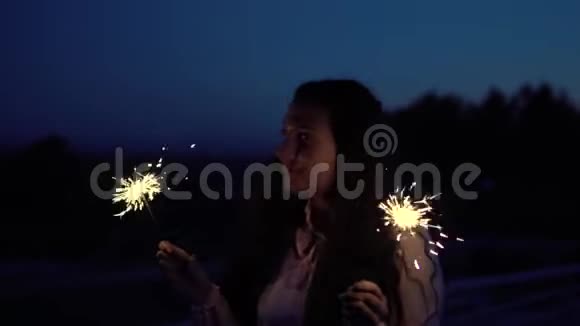 年轻女孩穿着长发手里拿着烟火站在一个夜晚城市的背景上拥有一个美好的夜晚视频的预览图