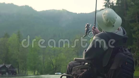 在森林和高山附近美丽的湖泊中残疾渔民在电动轮椅上慢动作捕鱼视频的预览图
