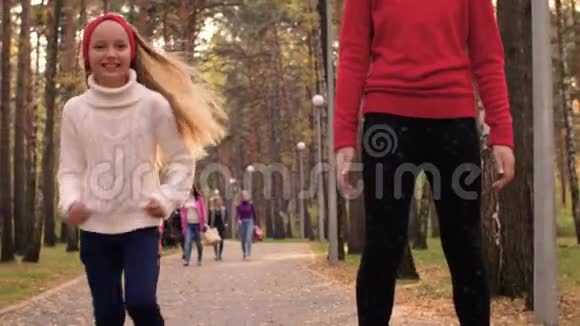 年轻快乐的女孩一起慢动作在秋天公园的路上奔跑视频的预览图