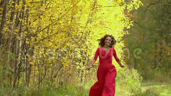 美丽的女孩穿着红色的裙子在森林里有健康的长发快乐的女人在秋天慢动作微笑120英尺视频的预览图