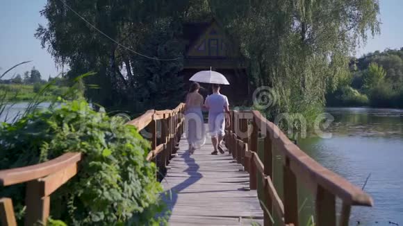 恋爱中的男人和女人用白色的伞走在一座木桥上视频的预览图