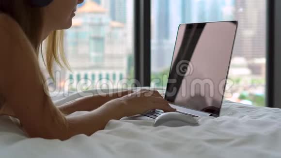 一位躺在床上的年轻女性自由职业者用无线耳机听音乐并开始工作视频的预览图