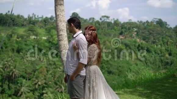 新婚夫妇在巴厘岛悬崖附近摆姿势牵手拥抱浪漫的婚礼视频的预览图