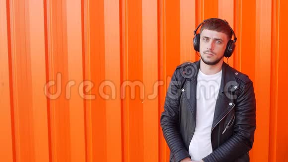 积极的年轻白种人站在音乐耳机里看着橙色背景下的摄像机视频的预览图