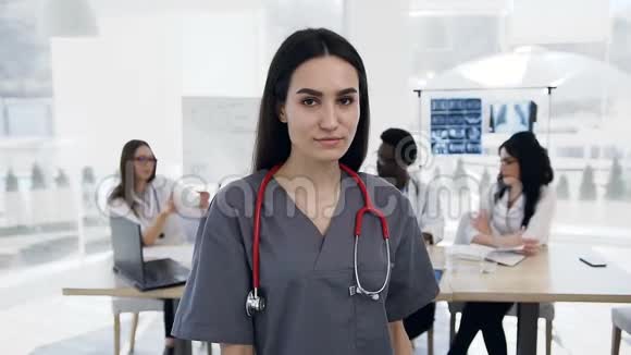 女医生看着镜头交叉双手而工作人员在医院的背景工作视频的预览图