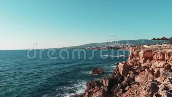 无人机飞过塞浦路斯的悬崖和岩石海滩地平线上有山脉海浪撞击着岩石海岸和海滩航空公司视频的预览图