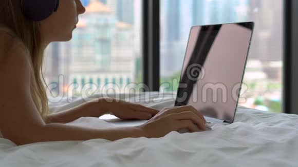 一位躺在床上的年轻女性自由职业者用无线耳机听音乐并开始工作视频的预览图