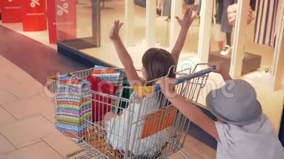 季节性的销售快乐的孩子们坐在购物中心的手推车里经过精品店的橱窗视频的预览图