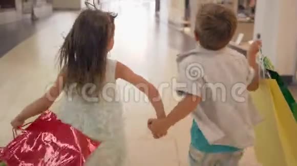 一个小男孩和一个女孩手里拿着很多购物袋在购物季节从商店橱窗里跑过去视频的预览图