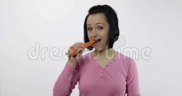 年轻漂亮的女人在白色背景下吃大胡萝卜傻笑视频的预览图