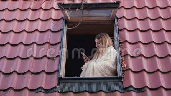 女人站在房子的屋顶窗户用电话视频的预览图