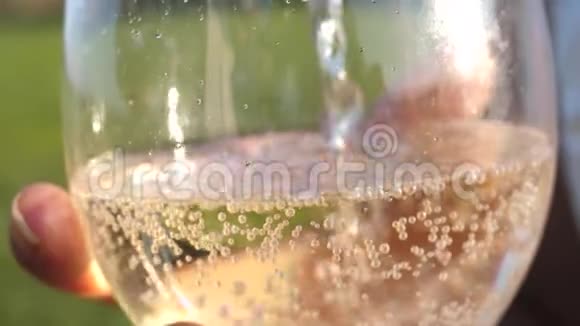 将瓶中的起泡葡萄酒倒入透明玻璃杯中特写镜头香槟在阳光下闪闪发光慢慢视频的预览图