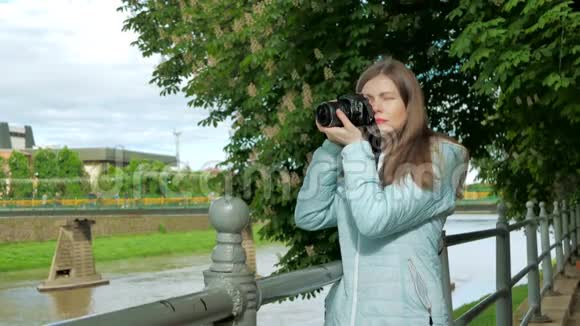 美丽的年轻女孩摄影师游客在河边的栏杆附近用专业相机拍照视频的预览图