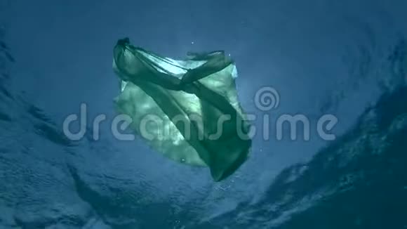 丢弃的绿色塑料袋在阳光下的蓝色水面下漂流海洋的塑料污染视频的预览图