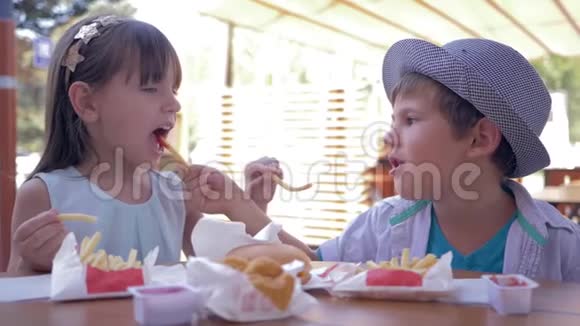 孩子们关心可爱的孩子们互相喂食快餐坐在街头咖啡馆的桌子上视频的预览图