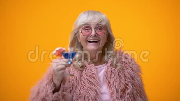 穿着粉色滑稽服装喝蓝色鸡尾酒的开朗的老年女士视频的预览图