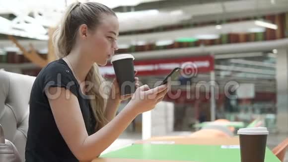 金发女人坐在大商场的桌子旁喝着茶拿着电话视频的预览图