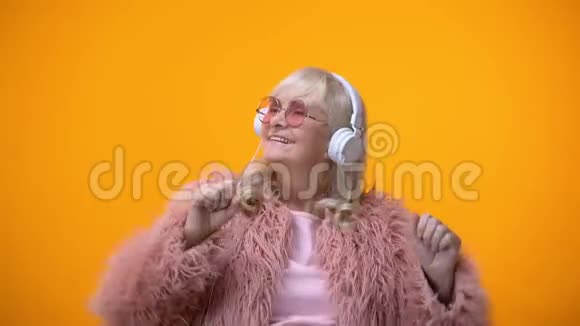 穿着粉红色外套和圆形太阳镜的积极的老年女士听音乐视频的预览图