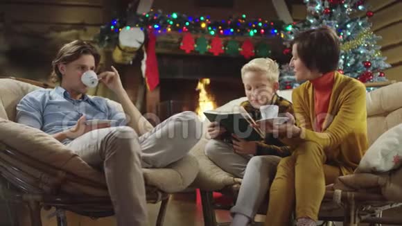 小男孩在圣诞节晚上一边读书一边哥哥和妈妈一边喝咖啡一边聊天视频的预览图