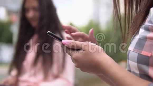在阳光明媚的天气里两个年轻女孩坐在喷泉附近的公园里用智能手机和平板电脑慢动作高清关闭视频的预览图