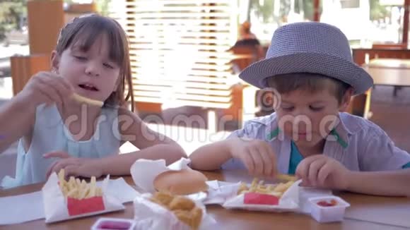 在快餐店吃东西的时候快乐的小男孩和小女孩一起玩垃圾食品视频的预览图